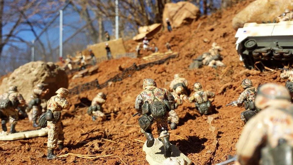 A collection of toy soldiers advancing across an outdoor hillside diorama